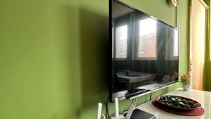 Ein modernes Wohnzimmer mit einem an der Wand befestigten Flachbildfernseher, einem weißen Tisch mit einer roten Tischmatte und einem kleinen Topfpflanz auf einem Holzboden.