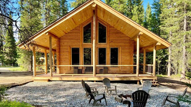 Eine Holzhütte mit Veranda, Sitzgelegenheiten im Freien und einer Schotterauffahrt.