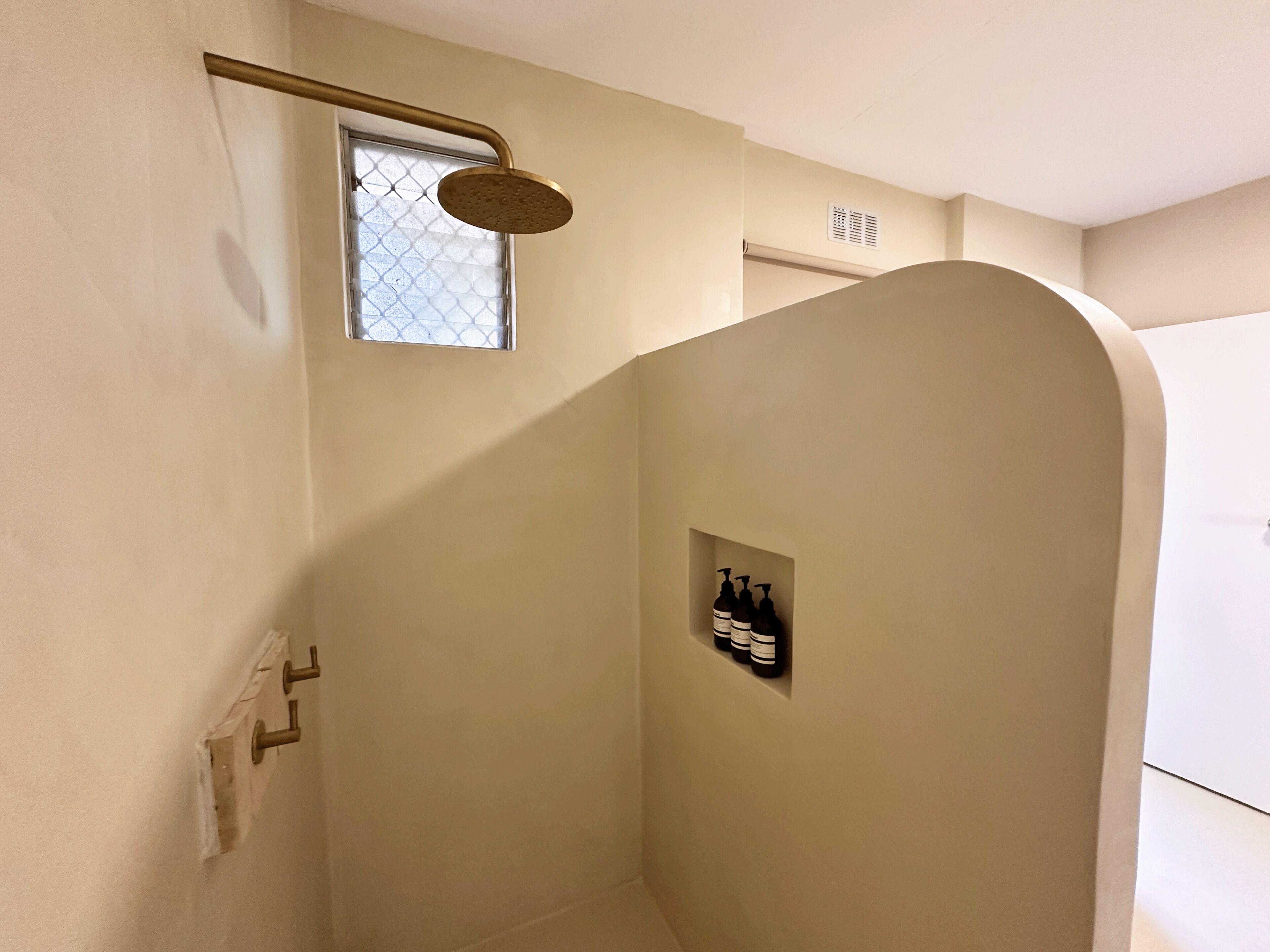 Une douche équipée d’un pommeau de douche à main, une petite fenêtre et une étagère pour les articles de toilette.