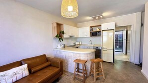 Una cocina moderna con armarios blancos, una isla central, taburetes de madera y una lámpara colgante.