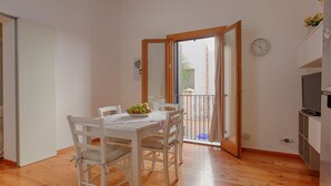 Un coin repas avec une table et des chaises, un petit balcon avec vue et un téléviseur posé sur un meuble.