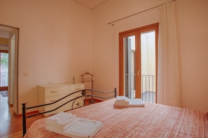 A bedroom with a bed, a dresser, a window with curtains, and a balcony.