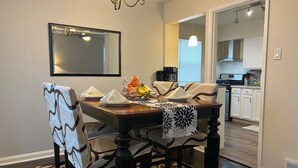 Un coin repas avec une table en bois, des chaises et un lustre. On aperçoit une cuisine au fond.