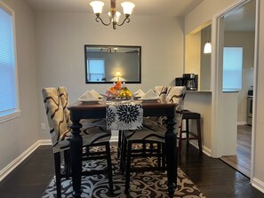 Un coin repas avec une table dressée pour quatre personnes, un lustre et un miroir au mur.