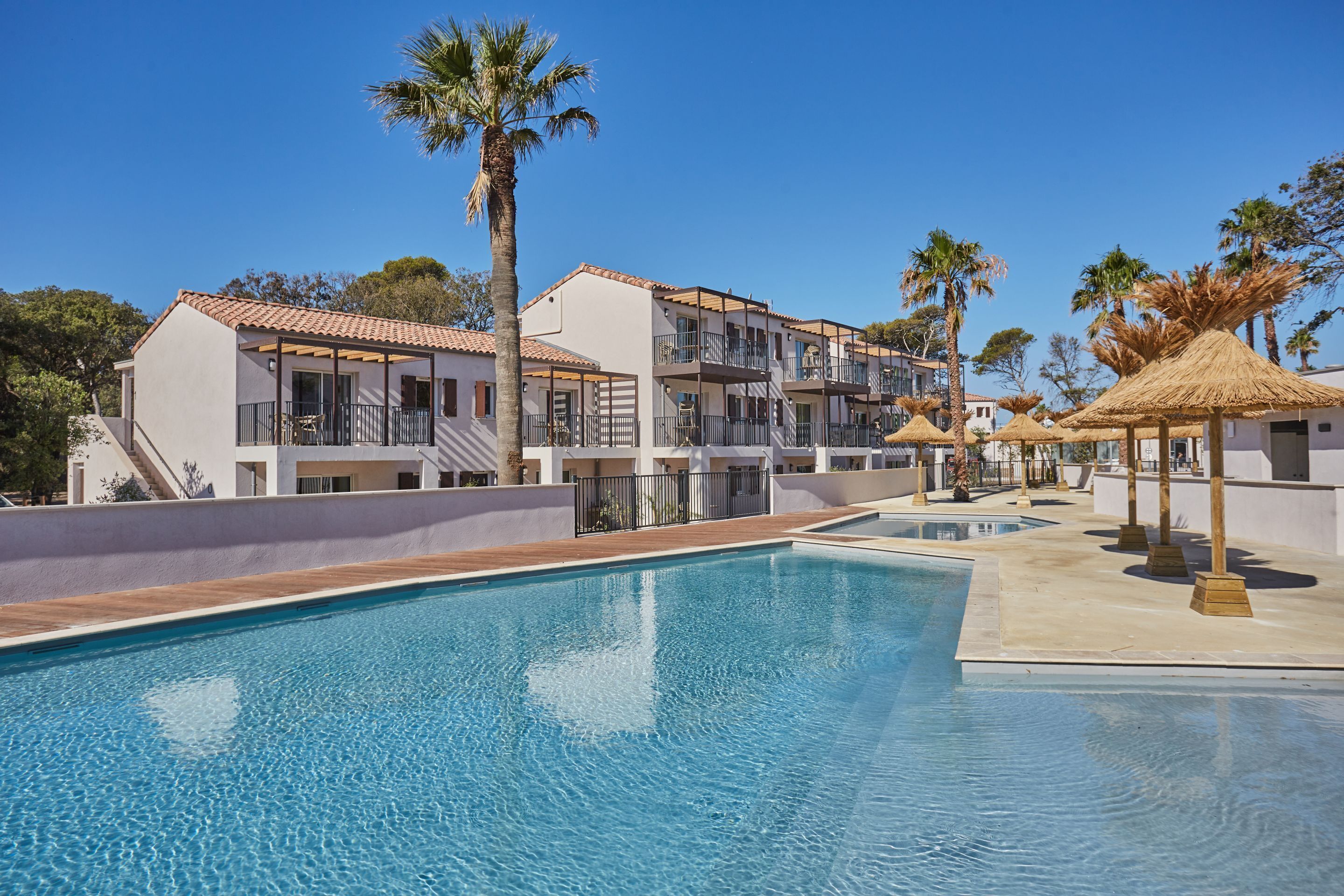 A hotel with a swimming pool, palm trees, and a clear blue sky.