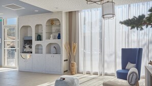 Een moderne woonkamer met een blauwe fauteuil, een witte poef en een keuken met witte kasten en een inbouwplank.