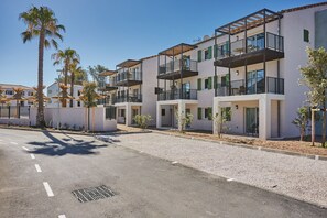 A modern multi-story residential building with balconies, a gravel driveway, and palm trees. - T4 moderne | Plage La Bergerie à 650m | Piscine (Hyères)