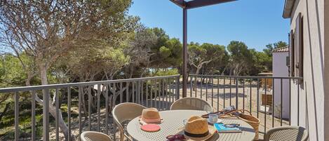 Un espacio de estar cubierto al aire libre con sillas de mimbre y una mesa redonda, con vistas a una playa de arena y árboles.