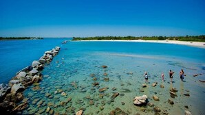Une plage dégagée, avec une côte rocheuse et quelques personnes debout dans une eau peu profonde.