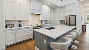 Une cuisine moderne avec des meubles blancs, un îlot central doté de tabourets de bar, un four encastré et un réfrigérateur en acier inoxydable.