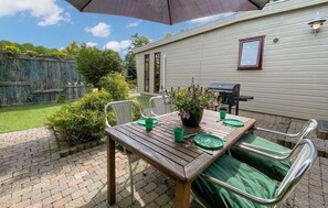 A wooden patio table with green chairs, a barbecue grill, and a potted plant.