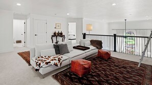 A spacious living room with a white sofa, a patterned rug, and leather poufs. - Home in Midway - Short Drive to Deer Valley Gondola | Mountain Views | Large Deck | Private Bedrooms (Midway)
