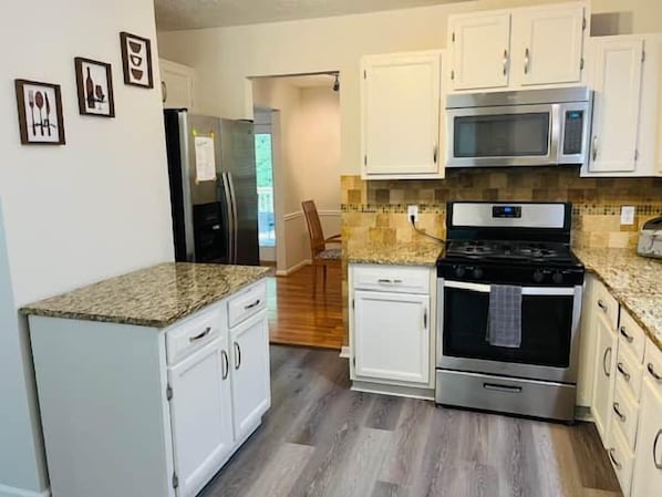 A kitchen with white cabinets, a stainless steel refrigerator, a microwave, a stove, and a dishwasher.