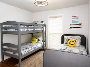 A bunk bed with a floral-patterned mattress, a single bed with a similar floral-patterned mattress, a wall-mounted arrow decoration, and a ceiling fan.