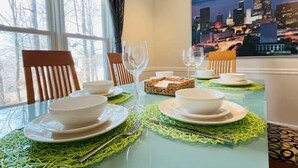 Een eettafel gedekt met borden, kommen en bestek, met uitzicht op een stadslandschap door een raam.