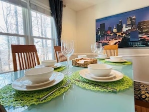 Een eettafel gedekt met borden, kommen en bestek, met uitzicht op een stadslandschap door een raam.