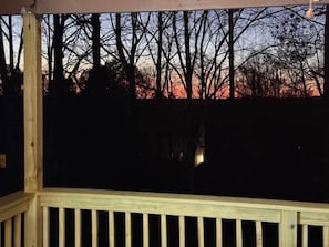 A wooden deck with a railing, overlooking a forested area.