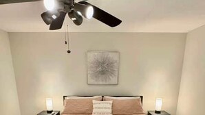 Een slaapkamer met een bed, twee nachtkastjes, een plafondventilator en een wandlamp.