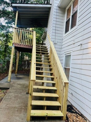 A wooden staircase leading to a covered outdoor area, adjacent to a white building with windows.
