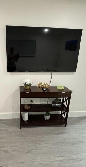 A flat-screen TV mounted on a wall above a wooden TV stand with decorative items. - Serenity Haven 2BR|1BA | Spacious | Free Parking (Miami)