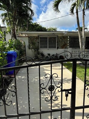 A gated entrance with a concrete pathway leading to a building with barred windows and a white exterior. - Serenity Haven 2BR|1BA | Spacious | Free Parking (Miami)