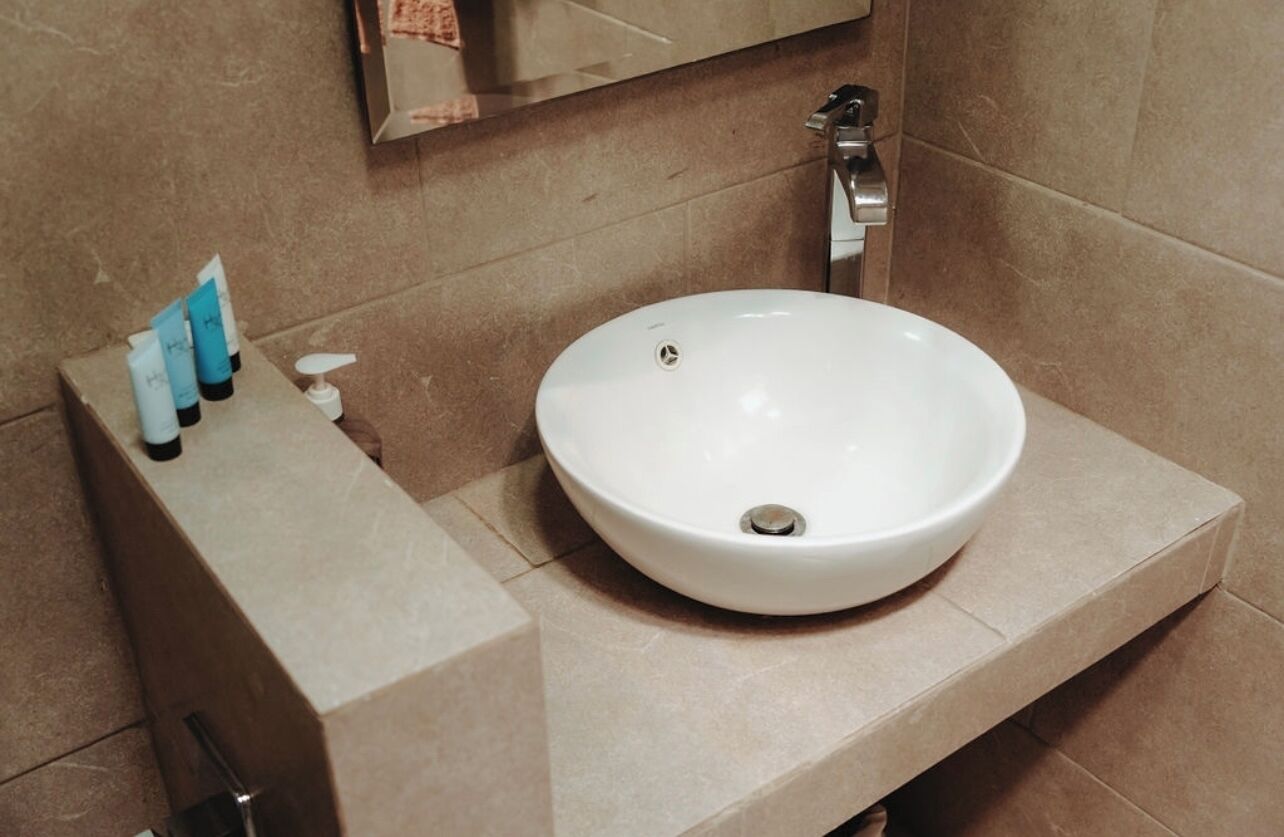 Et badeværelse med en hvid vask, et spejl og toiletartikler på en hylde.