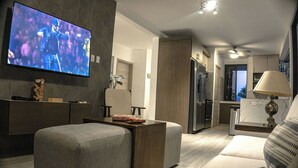 Una sala de estar moderna con un televisor de pantalla plana, un sofá, una mesa de centro y una cocina al fondo.