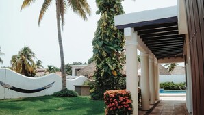 Un resort con un área exterior techada, palmeras y una piscina.