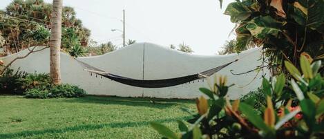 A hammock tied between two white walls in a garden with green grass and plants.