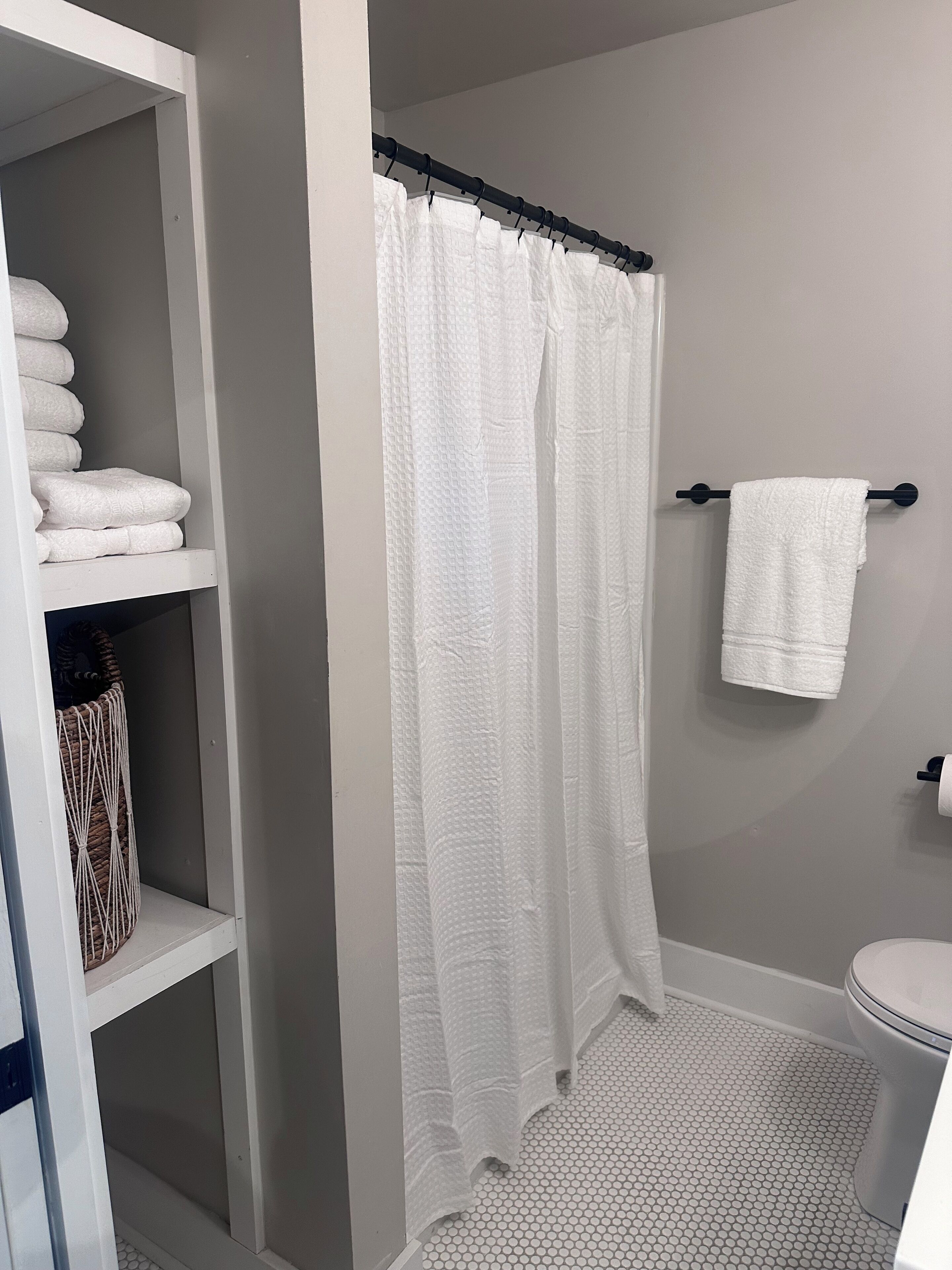A bathroom with a shower curtain, a towel rack, and a shelf with folded towels.