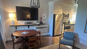 Una cocina moderna con electrodomésticos de acero inoxidable, un comedor con una mesa redonda y sillas, y un televisor montado en la pared.
