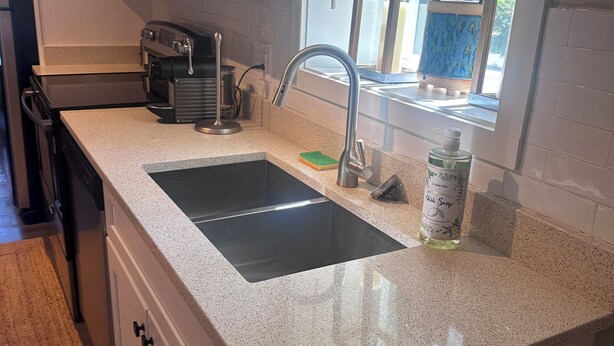 Una cocina moderna con un lavamanos de acero inoxidable, una cafetera y un ventanal con vistas a árboles.