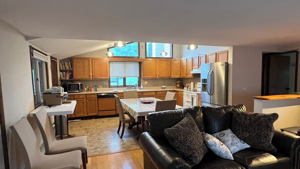 A modern kitchen with wooden cabinets, a stainless steel refrigerator, and a dining area with a table and chairs.