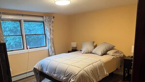A bedroom with a bed, a nightstand, a window with curtains, and a ceiling light.