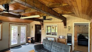 A spacious living area with a grey sofa, wooden ceiling beams, and a ceiling fan.