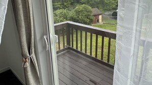 A room with a wooden deck and a view of a house and trees.