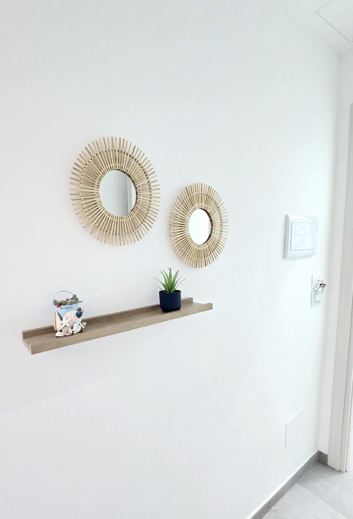 A hallway with two wall-mounted mirrors and a wooden shelf with decorative items and a plant.