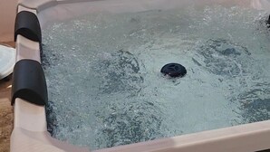 Un jacuzzi con panel de control, rodeado por un muro color crema y una vista despejada del cielo y edificios al fondo.