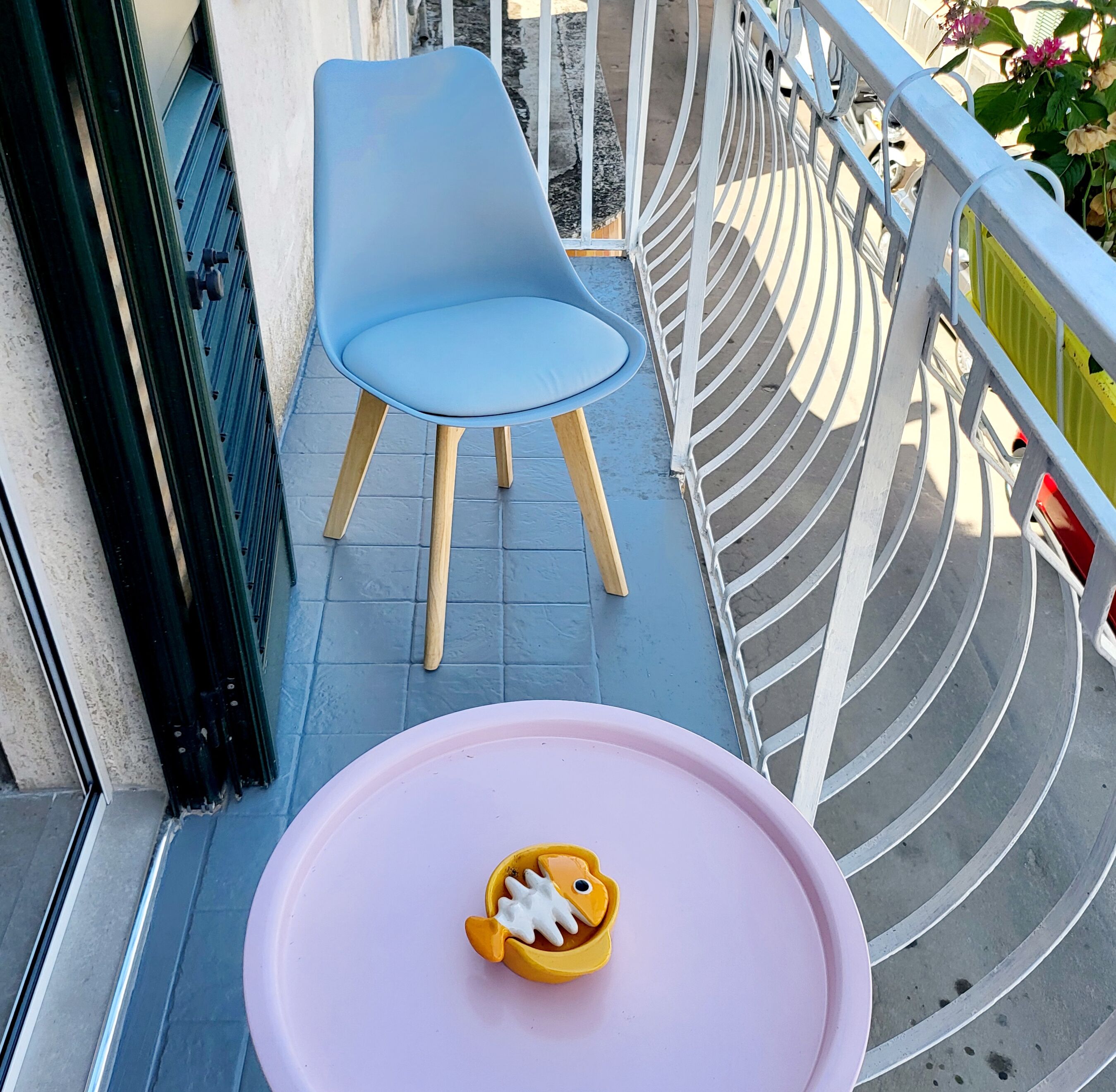A balcony with a blue chair and a pink table with a toy.