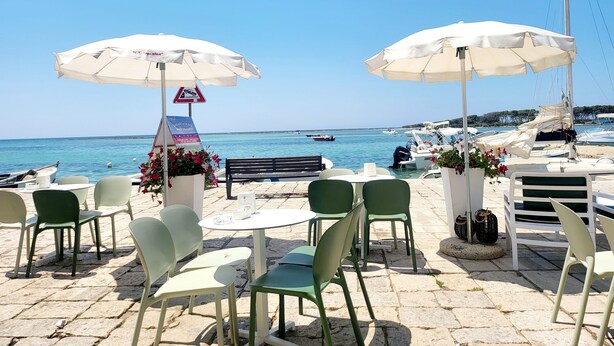 Un café junto al mar con terraza, sombrillas blancas y vistas al océano.