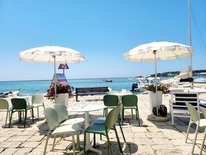 Un café junto al mar con terraza, sombrillas blancas y vistas al océano.