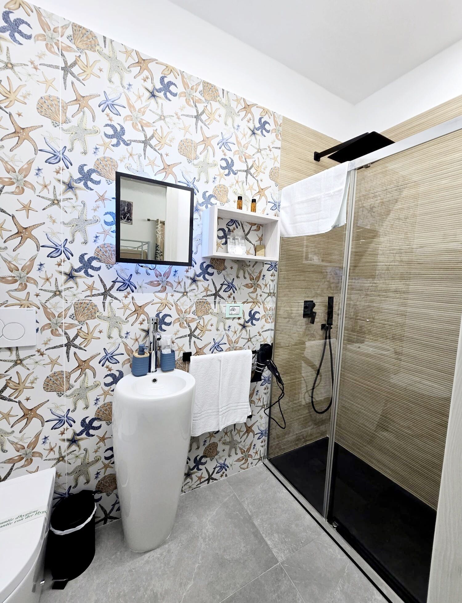 Un bagno con carta da parati a tema marino, un lavandino bianco, uno specchio e una cabina doccia.