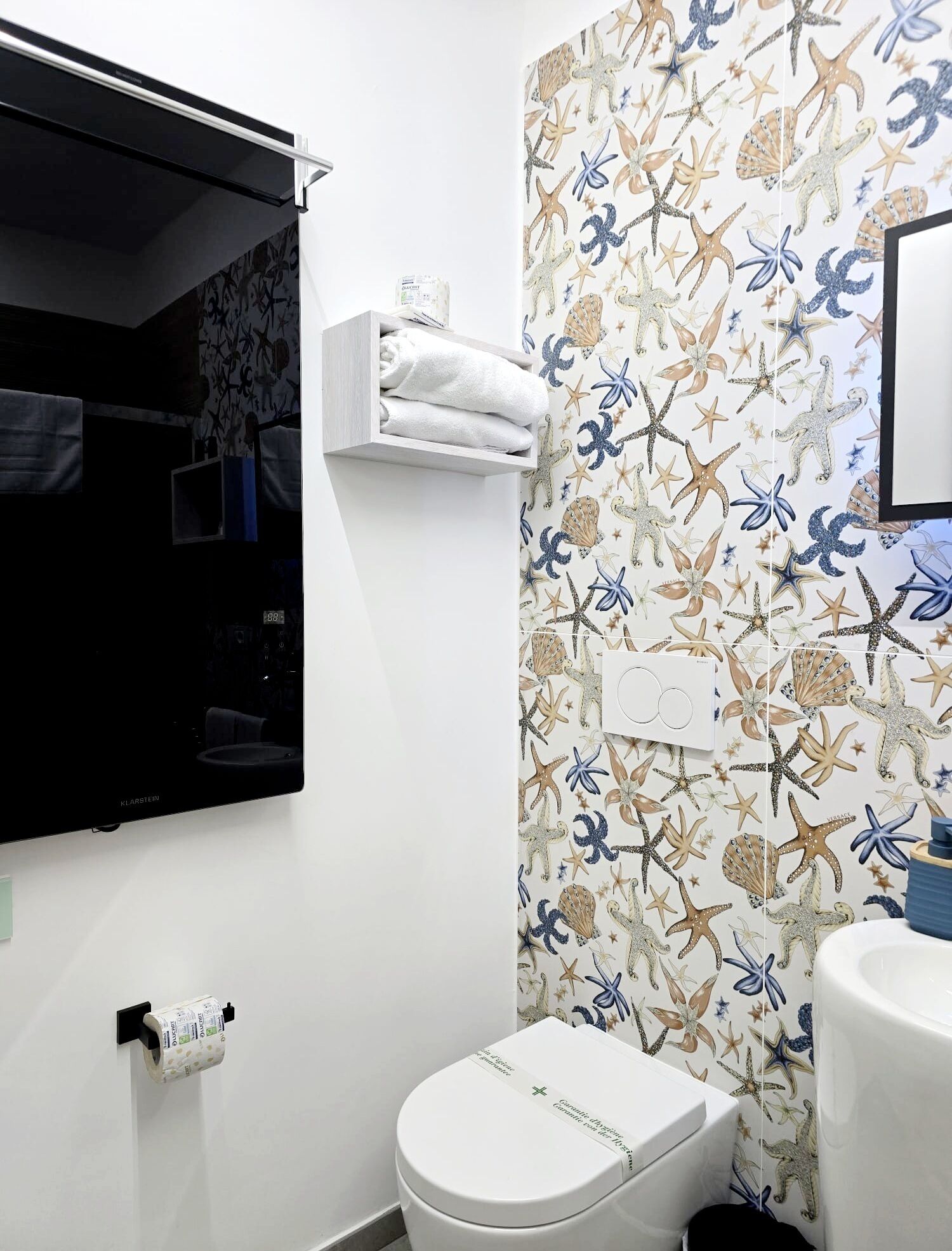 A bathroom with a toilet, a shelf with a towel, and a wall with a starfish pattern.