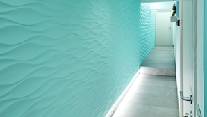 Un pasillo con una pared azul verdosa texturizada, piso de baldosas y una puerta con cerradura electrónica.