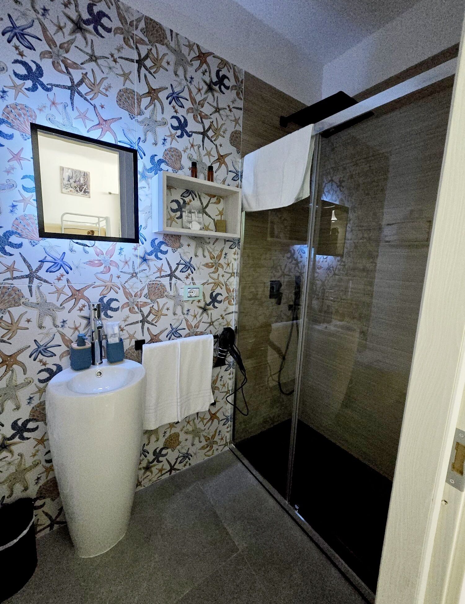 Une salle de bain avec un papier peint sur le thème de la mer, un lavabo avec un miroir et une douche à parois de verre.