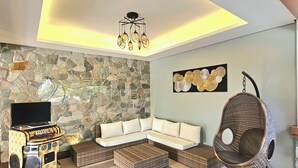 A modern living room with a stone wall, a sectional sofa, a hanging chair, and a unique entertainment unit. - The Backyard Event and Resorts (Candaba)