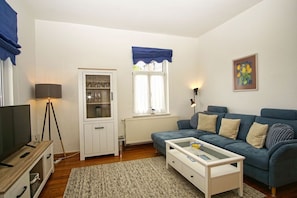 Una sala de estar con un sofá azul, un aparador blanco, una lámpara de pie y un cuadro en la pared.