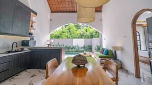 Eine moderne Küche mit dunklen Schränken, einem Holztisch und Blick auf üppiges Grün durch ein Rundbogenfenster.