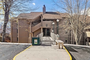 A building with a ramp leading to a door, a trash bin, and a bench.