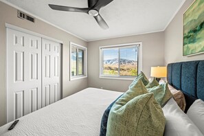 Ein Schlafzimmer mit einem Bett, einem Deckenventilator, einem Fenster mit Bergblick und einem Gemälde an der Wand.